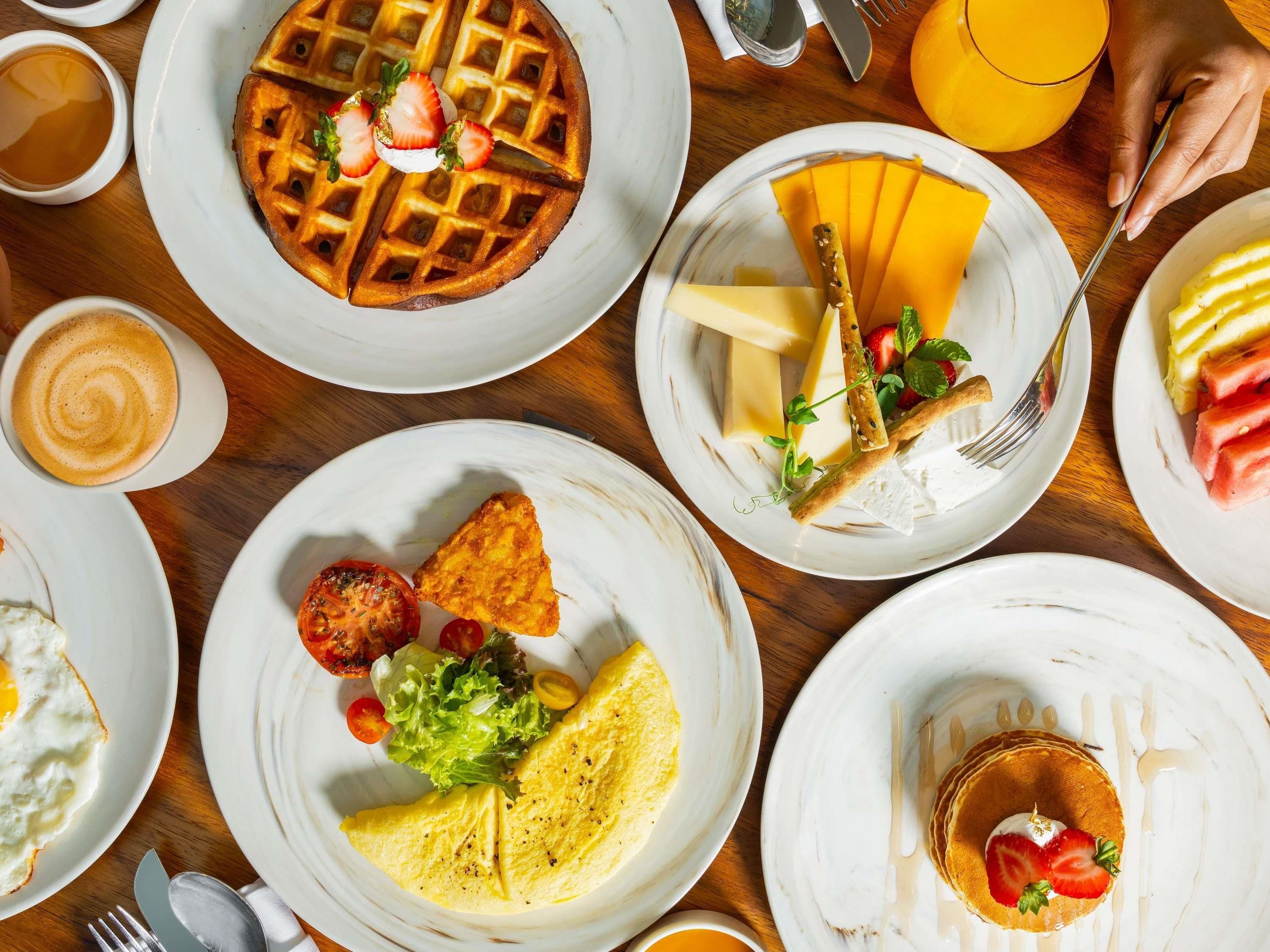 A breakfast buffet with waffles, omelets, and various fruits and cheeses.