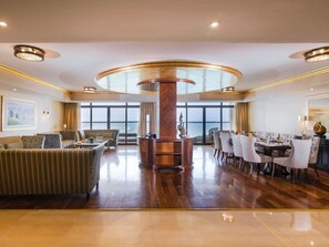 Un'ampia hall d'albergo con un pilastro centrale, un'area ristorazione con sedie bianche e un'ampia finestra che offre una vista.