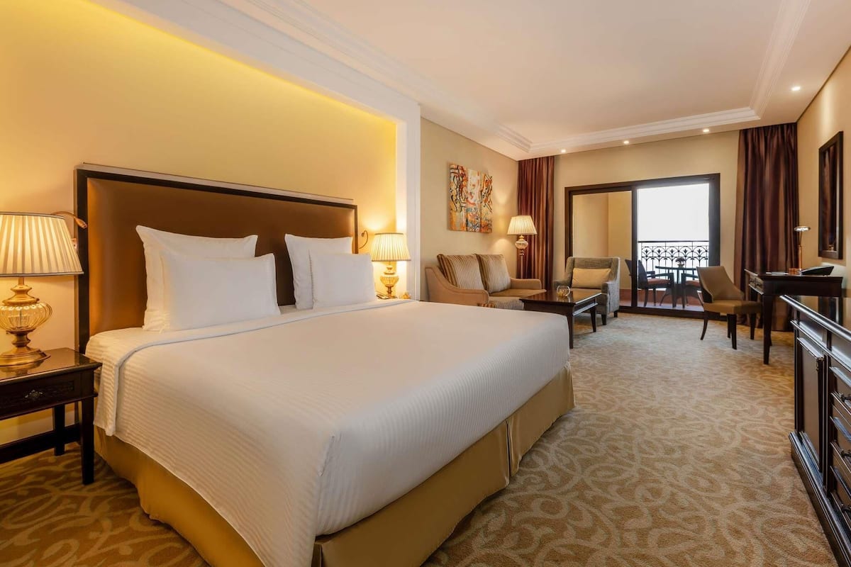 A hotel room with a large bed, a desk, a chair, and a balcony with a view.