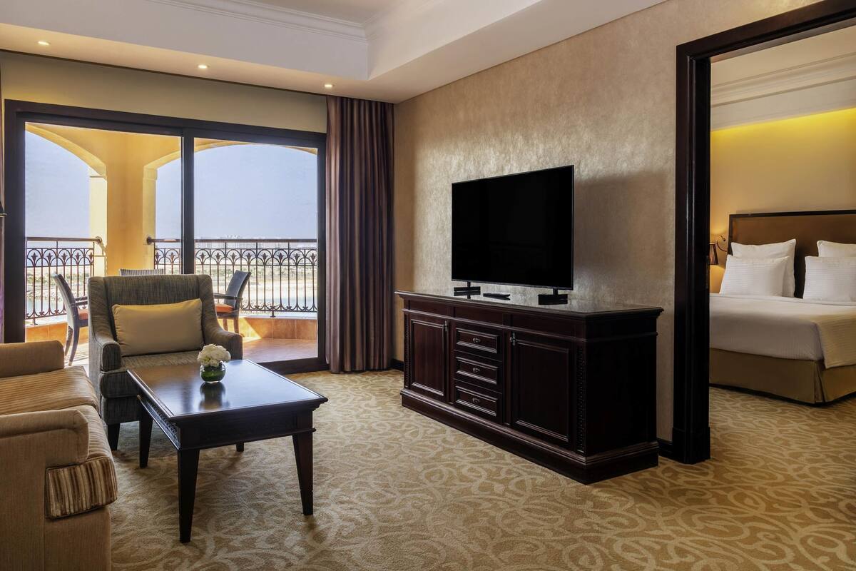 Une chambre d’hôtel avec un balcon, une télévision à écran plat, un lit, un canapé et une table basse.