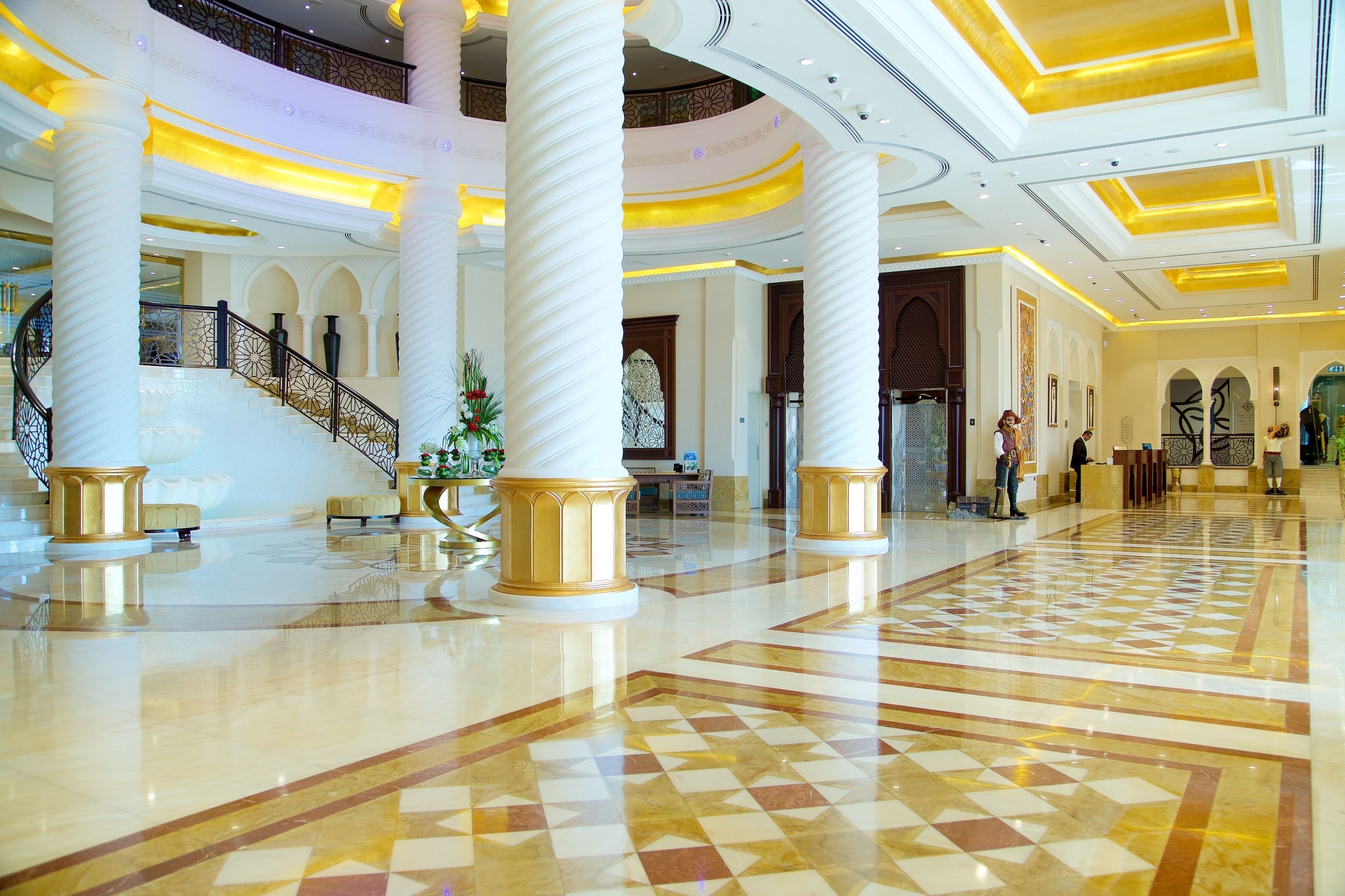 A spacious lobby with a checkered floor, large columns, a staircase, and a decorative staircase railing.