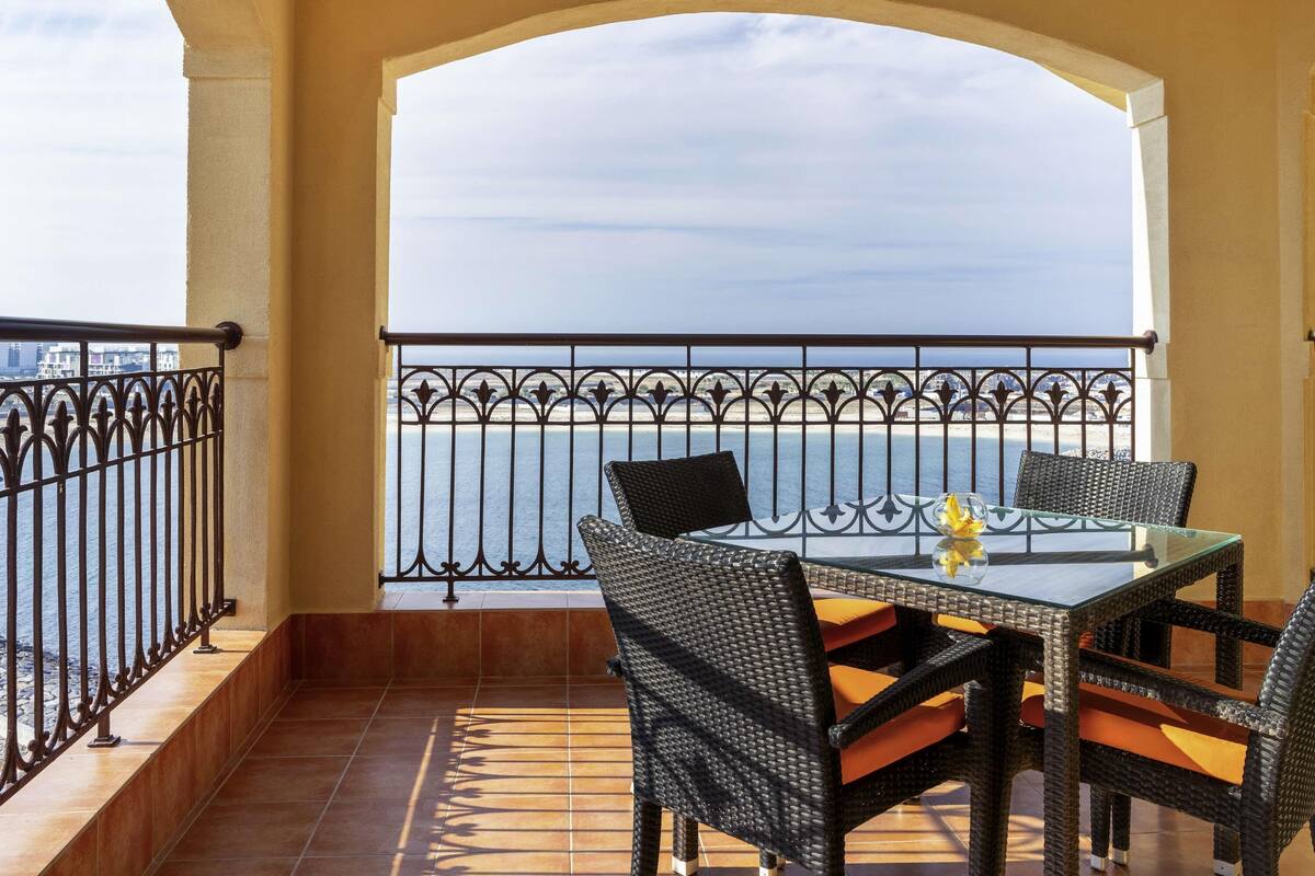 Un balcon avec une table et des chaises, une vue sur la mer et une balustrade.
