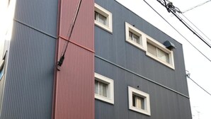 A multi-story building with a red and blue facade, a signboard for 'Guest House', and outdoor seating with chairs and a table. - IM Guest House - Hostel (Osaka)
