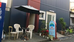 A guest house with a red and blue exterior, a small outdoor seating area with a table and chairs, and a bicycle parked nearby. - IM Guest House - Hostel (Osaka)