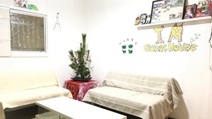 A room with two sofas, a glass coffee table, a small plant on a table, and a wall with a shelf displaying photos and books. - IM Guest House - Hostel (Osaka)