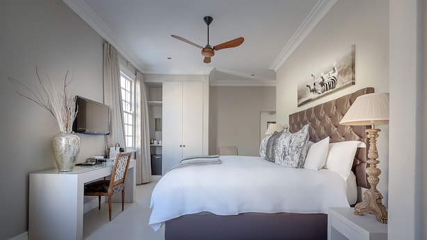 A bedroom with a large bed, a desk, a chair, a TV, and a ceiling fan. - Long Street Boutique Hotel (Cape Town)