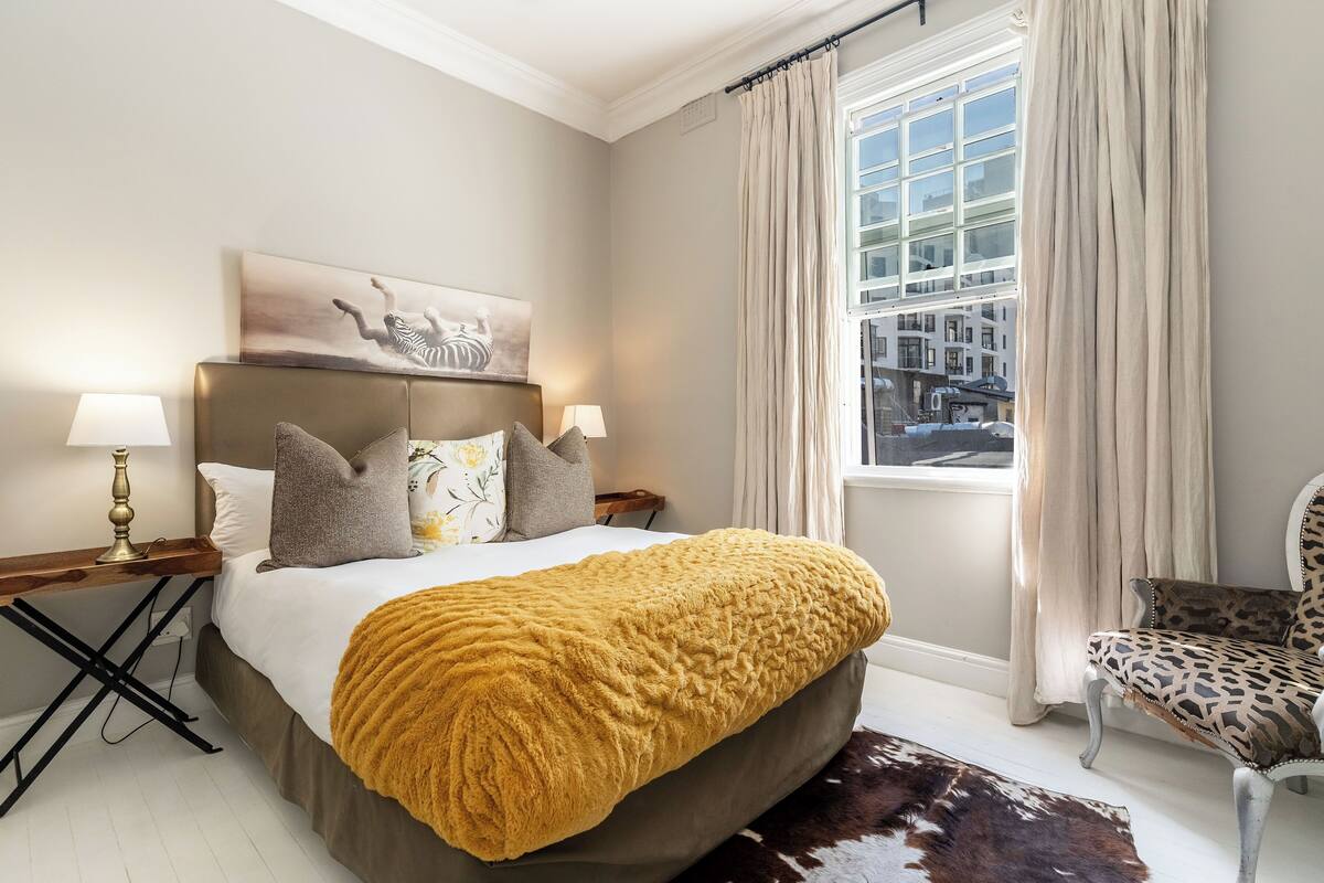 A bedroom with a large bed, a view of the city through a window, and a leopard print chair.