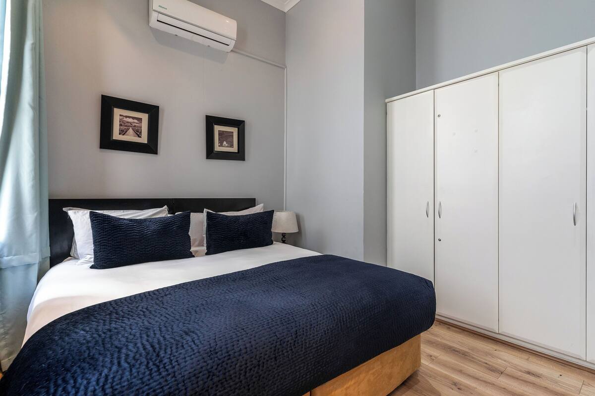 A neatly made bed with a dark blue blanket, a white headboard, and two framed pictures on the wall.