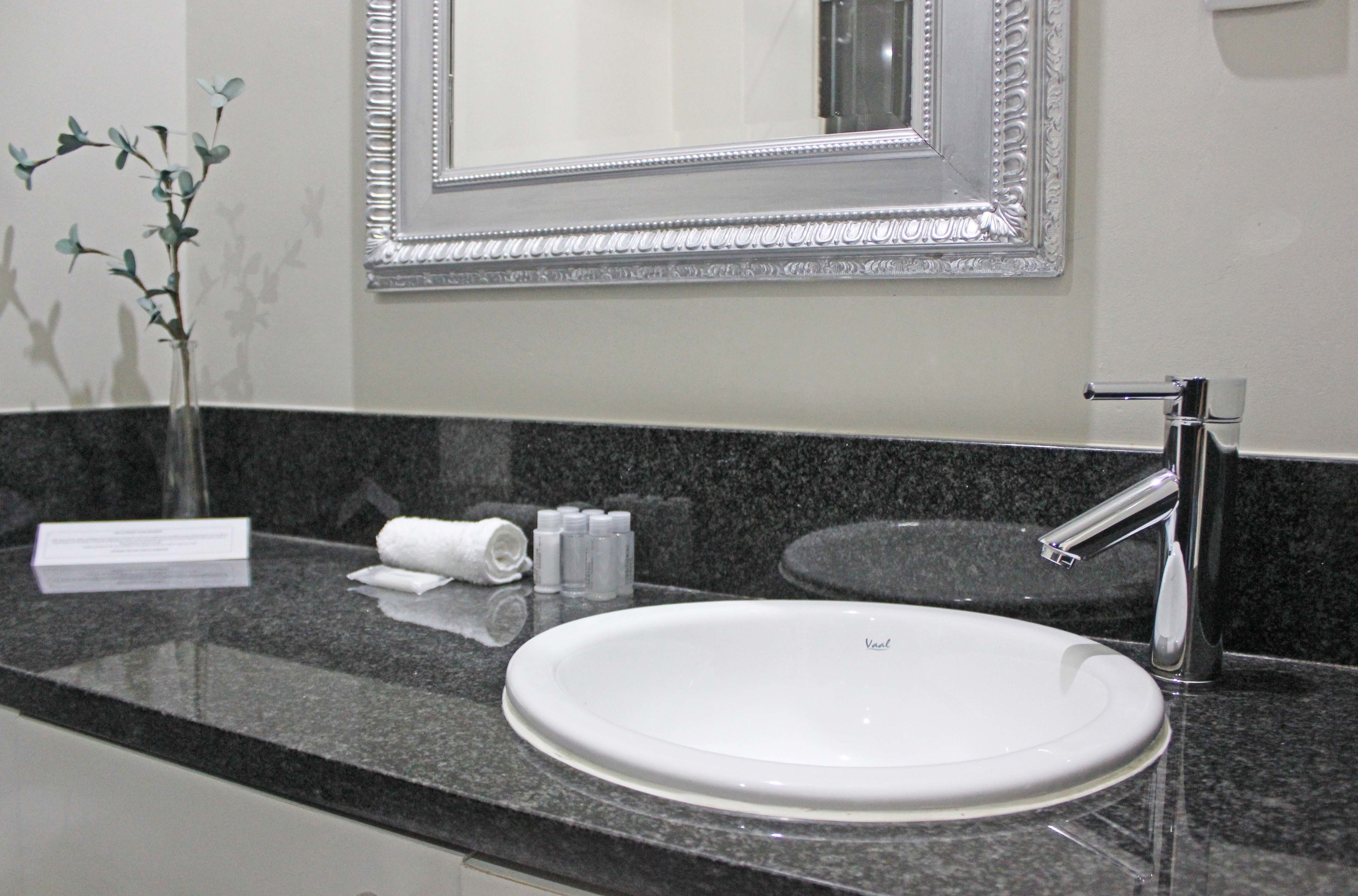 A bathroom with a white sink, a mirror with an ornate frame, and a vase with green leaves.