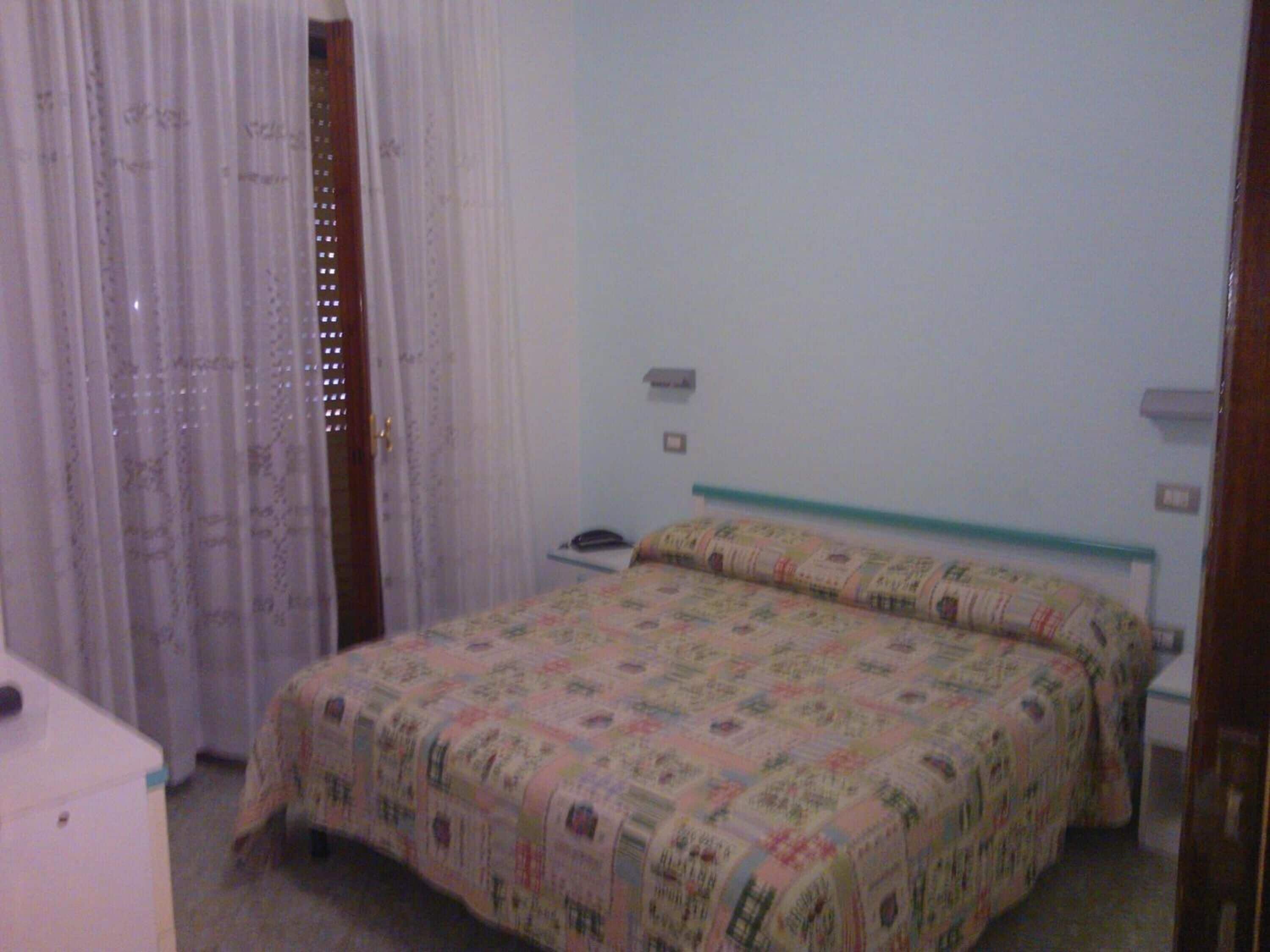 Una camera da letto con un letto, un comodino, un telefono e una finestra con tende.