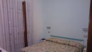 Una camera da letto con un letto, un comodino, un telefono e una finestra con tende.