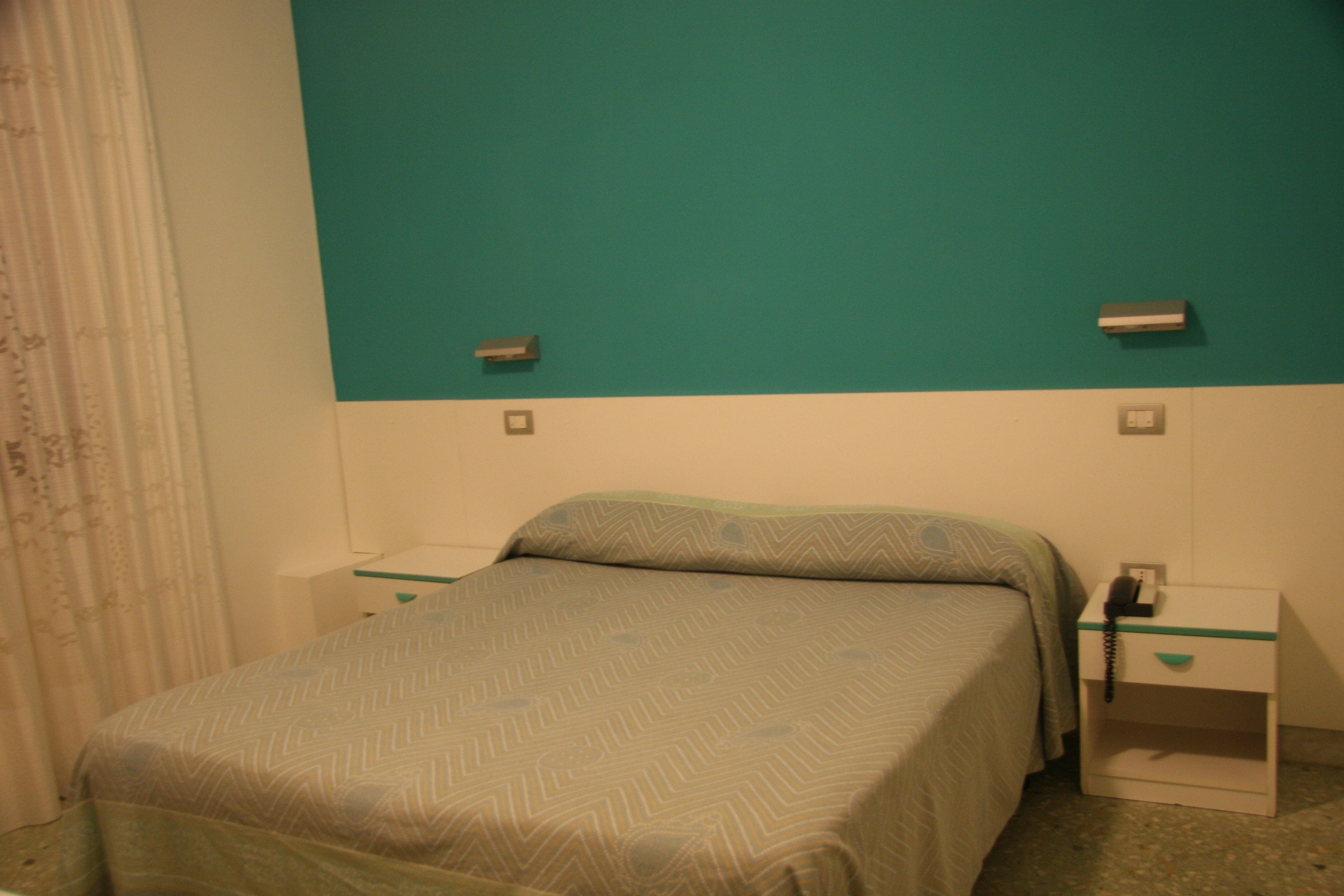 A room with a bed, a nightstand with a phone, and a wall-mounted light switch.