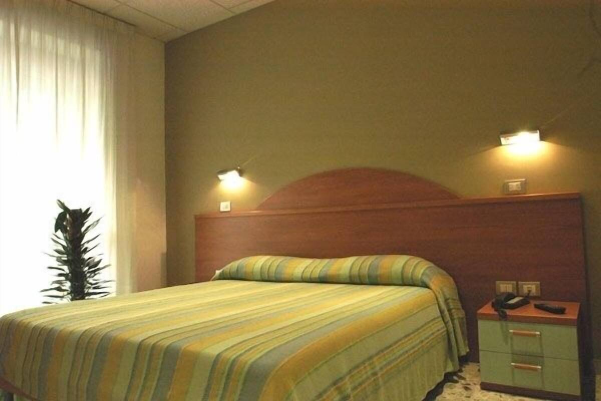 Una habitación de hotel con cama, mesita de noche, teléfono y lámpara de pared.