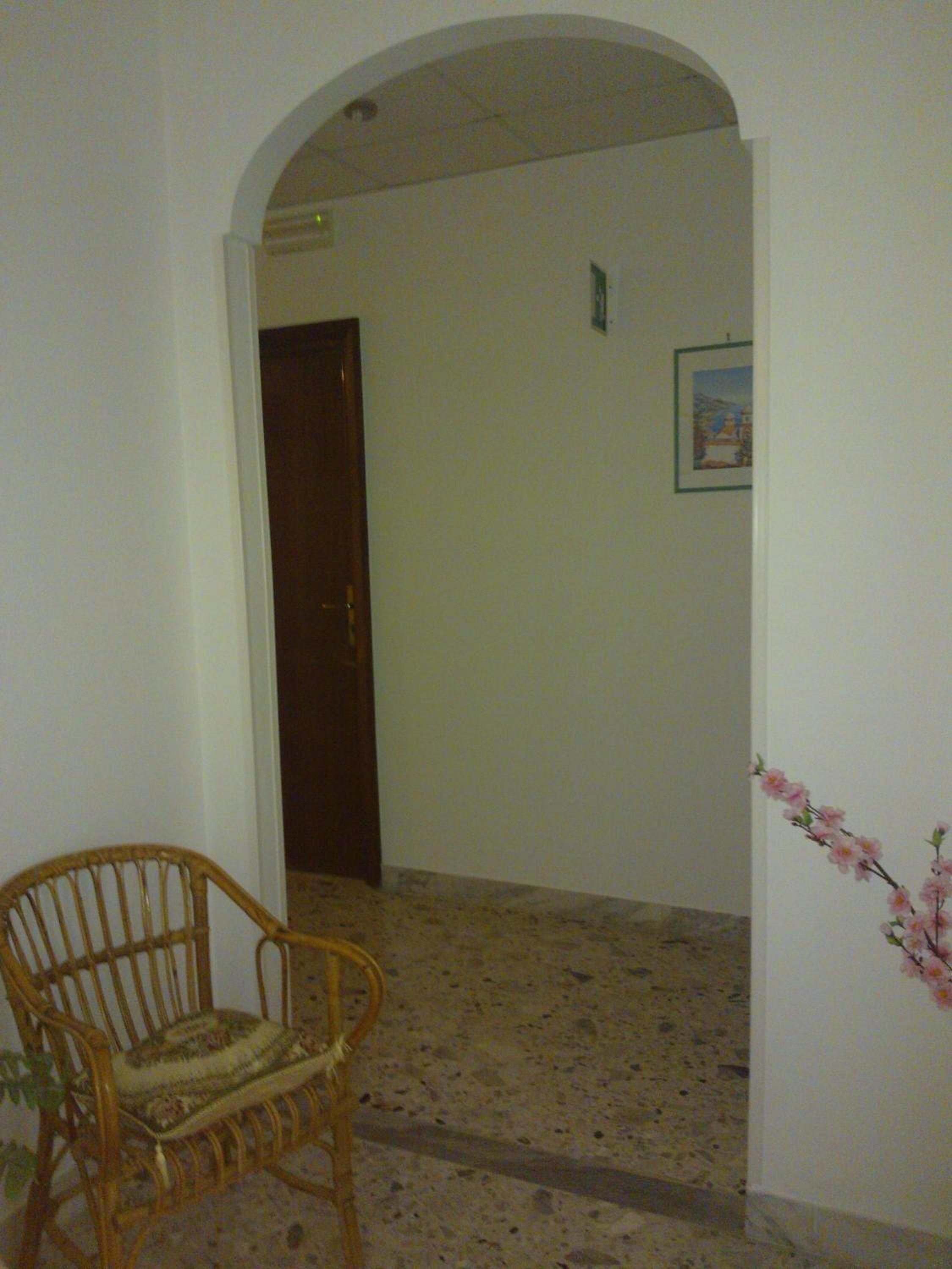 A hallway with a wooden chair, a door, and a framed picture on the wall.