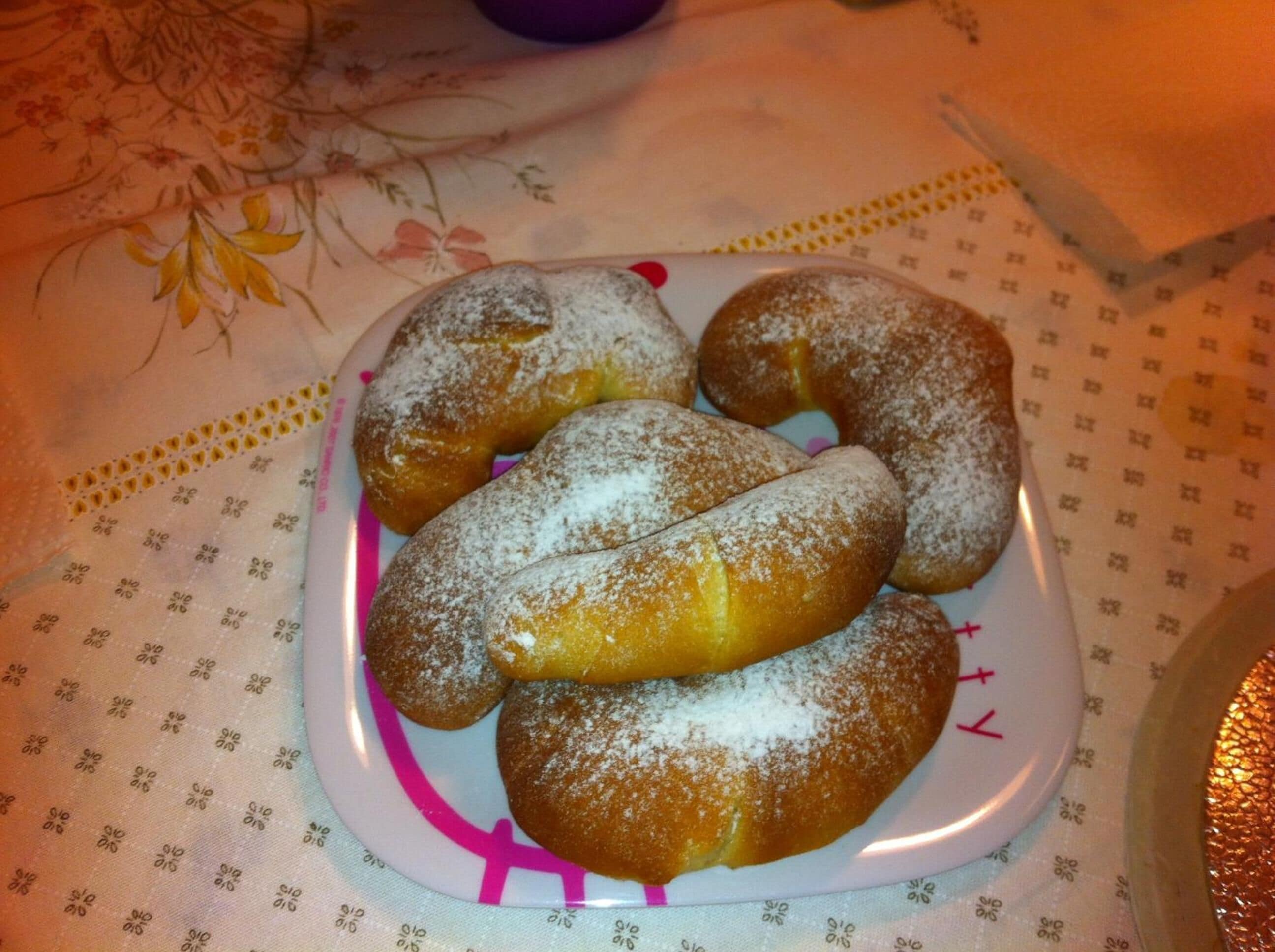 Une assiette de beignets saupoudrés de sucre, posée sur une table recouverte d’une nappe à motifs floraux.