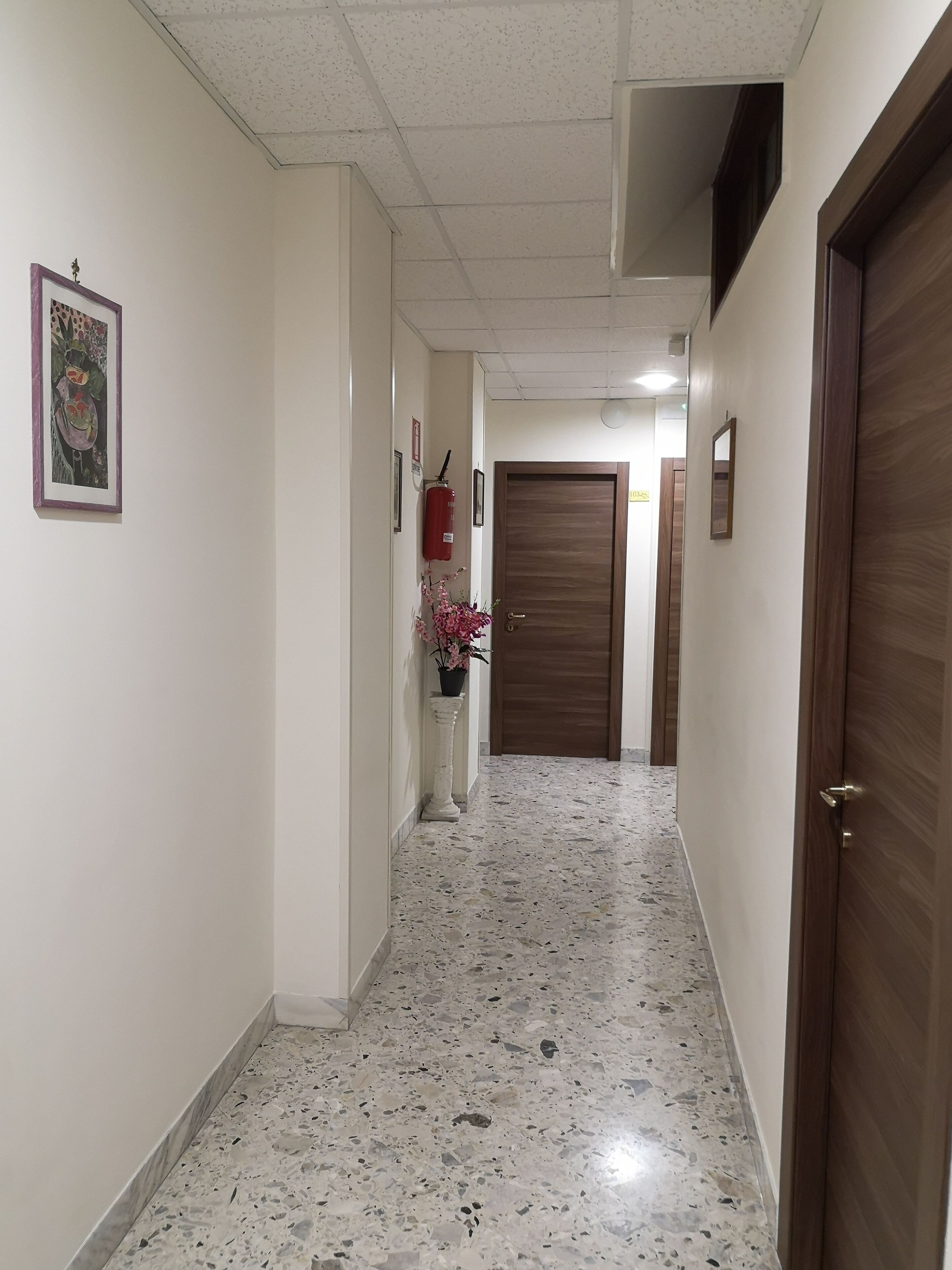 Un pasillo con piso de terrazo, una puerta de madera y un extintor en la pared.
