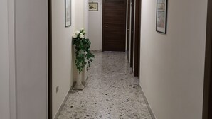 A hallway with a polished terrazzo floor, framed pictures on the walls, and a potted plant. - B&B Vittoria (Maiori)