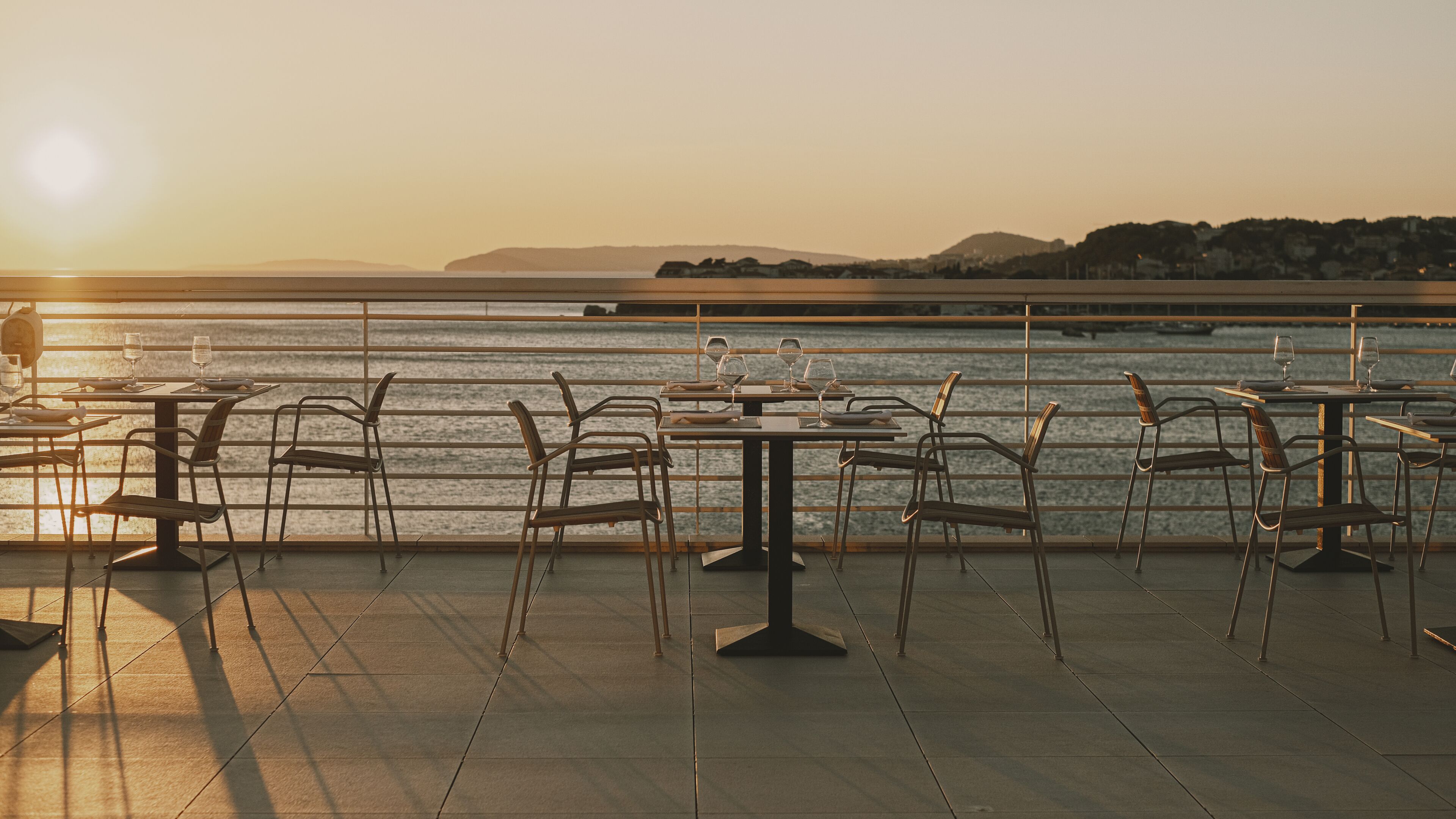 Un restaurant situé au bord de l’eau, avec des tables et des chaises, offrant une vue sur un plan d’eau et sur des collines lointaines.