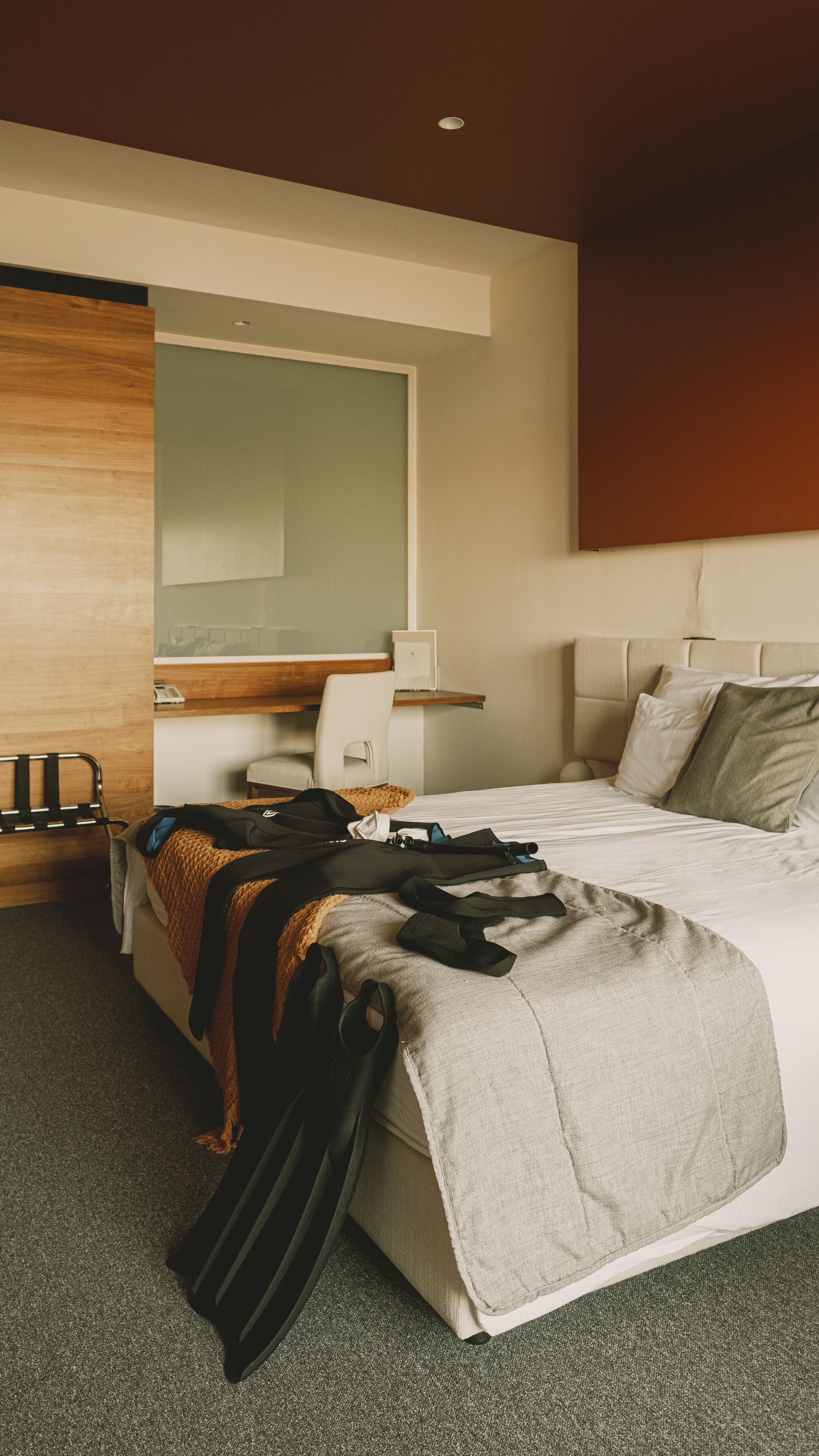 A hotel room with a bed, a desk, a chair, and a mirror.