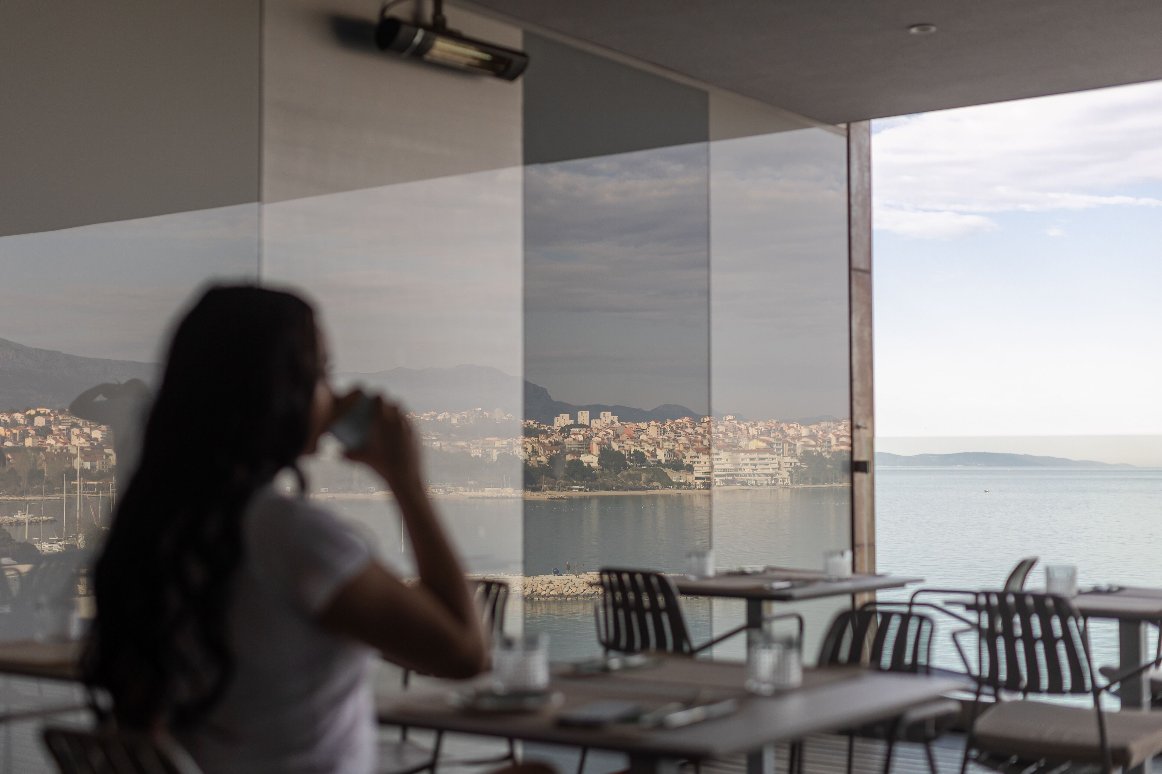 A woman sitting at a table with a view of a cityscape and water.