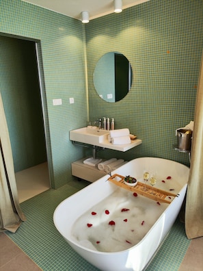 A bathroom with a bathtub filled with rose petals, a sink, a mirror, and a shower area.