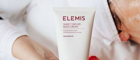 A person holding a tube of Elemis Sweet Orchid Body Cream.