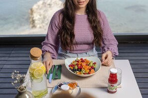 A person seated at a table with a bowl of fruit salad, a bottle of juice, and a glass of water.