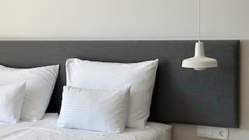 A modern bedroom with a bed, white pillows, a grey headboard, a hanging pendant light, and a small bedside table.