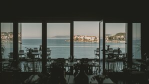 A restaurant with large windows overlooking a coastal view, featuring tables and chairs arranged for dining. - Hotel Split (Podstrana)