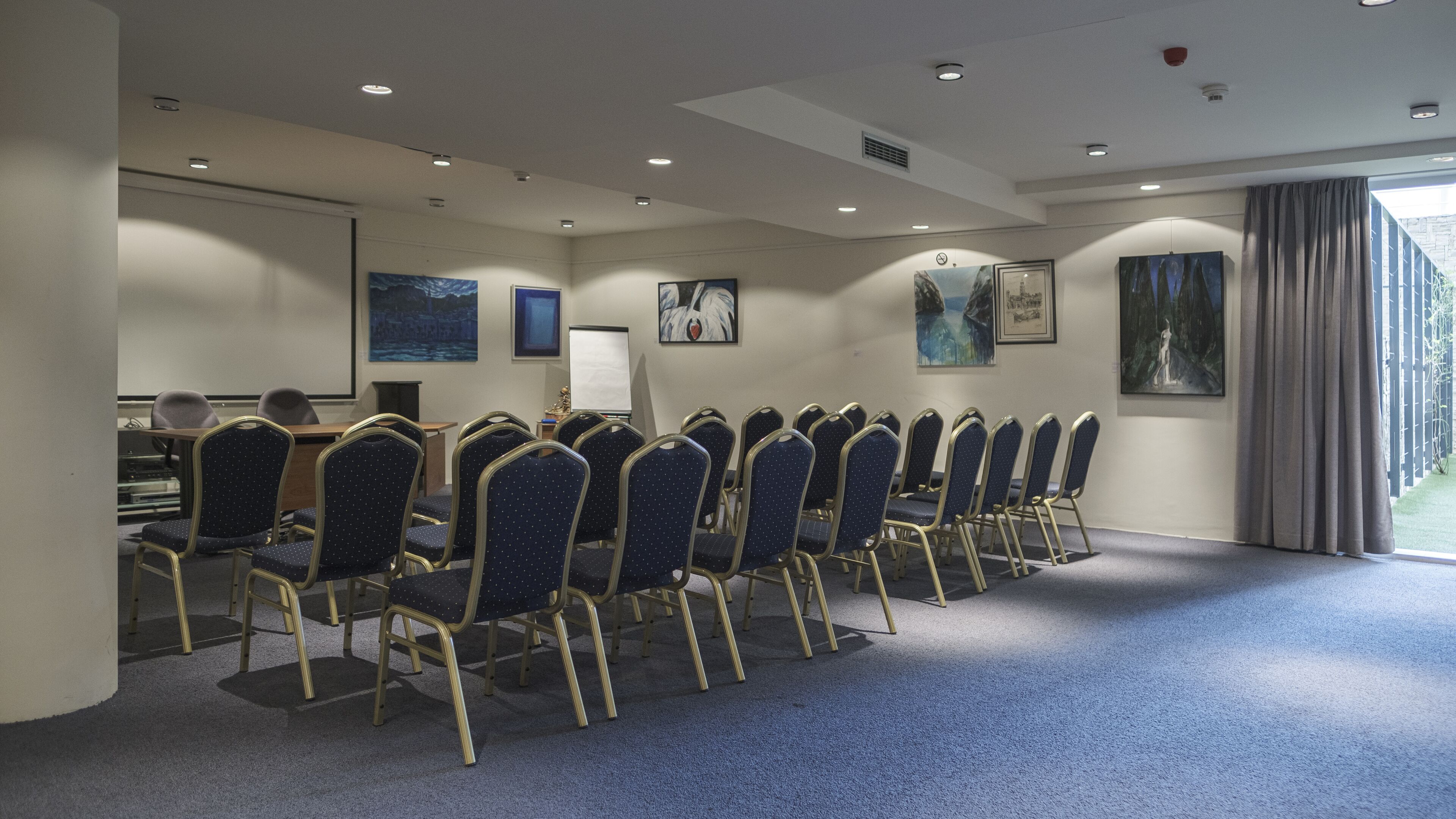 Ein Konferenzraum mit Reihen von Stühlen, einer Tafel und Kunstwerken an den Wänden.