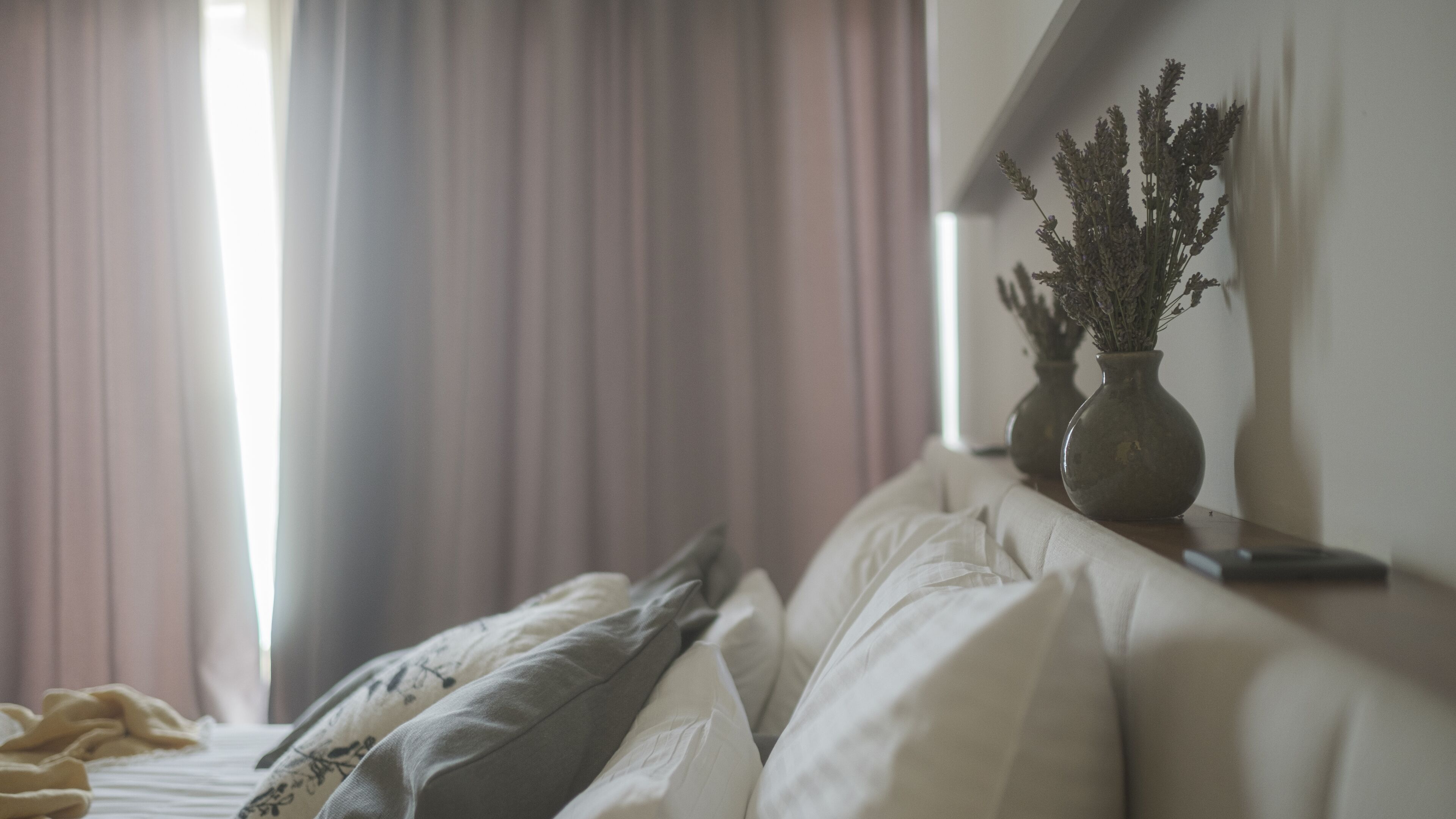 A bedroom with a bed, pillows, a nightstand, and a vase with dried flowers.