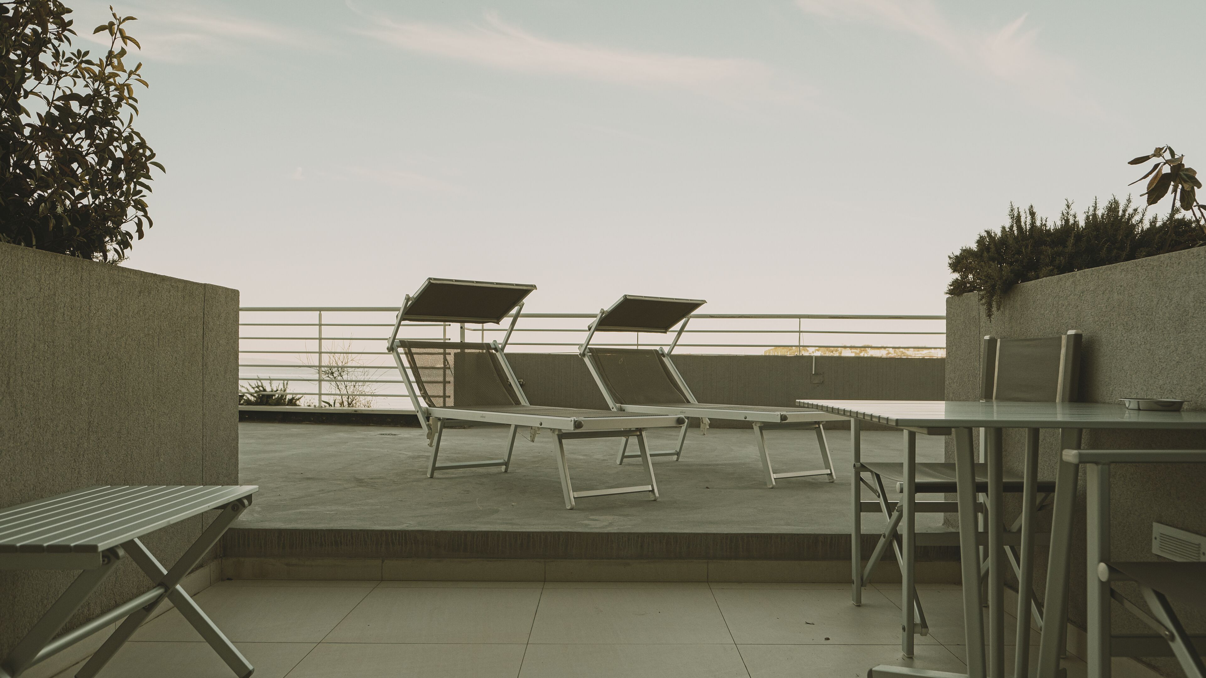 Terraza en la azotea con dos tumbonas y una mesa, rodeada por un muro bajo y una barandilla.