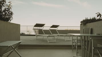 Terraza en la azotea con dos tumbonas y una mesa, rodeada por un muro bajo y una barandilla.