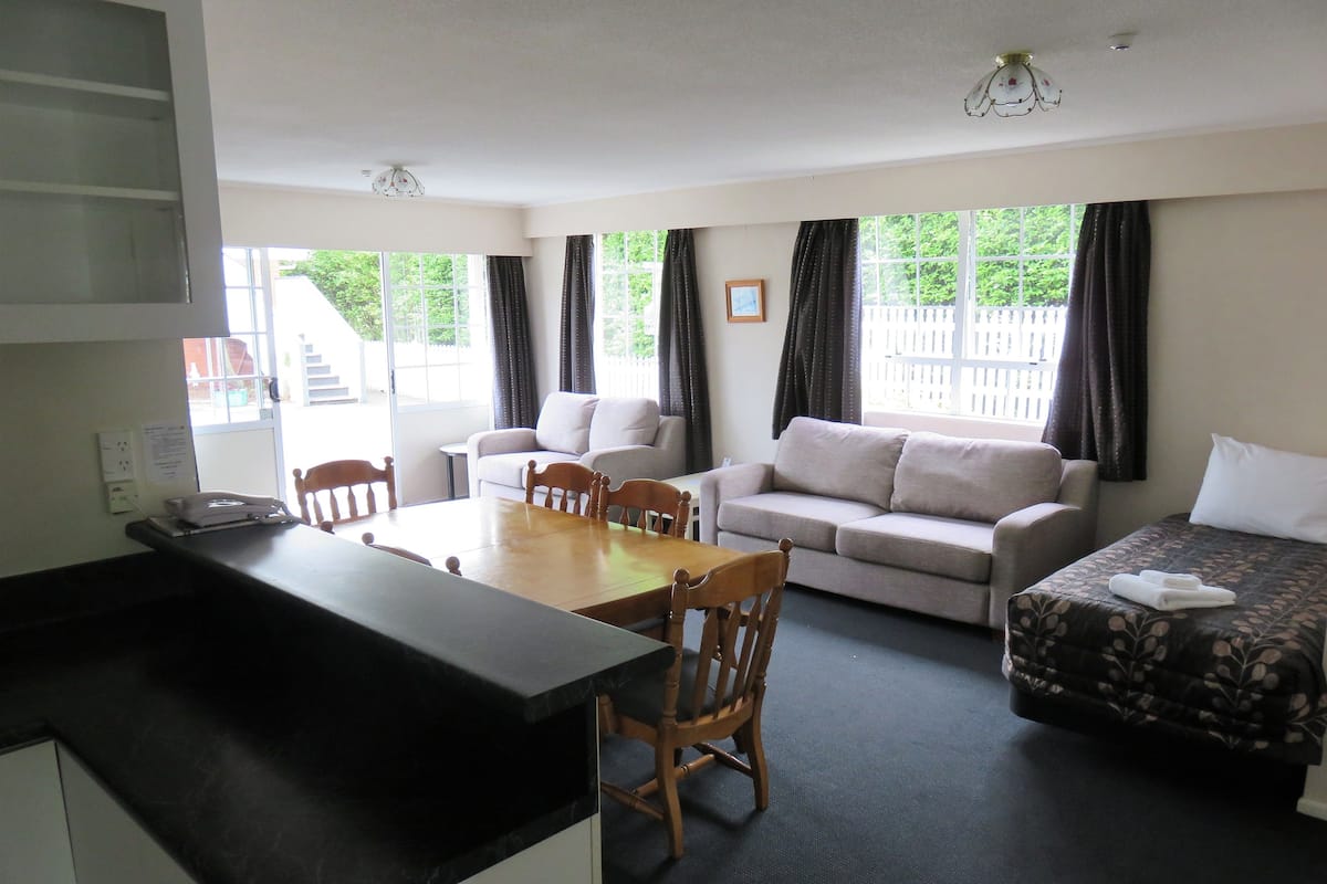 A compact living space with a kitchenette, a sofa, a dining table with chairs, and a bed with a floral bedspread.