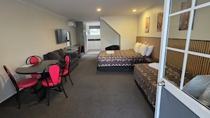 Habitación de hotel compacta con cama, escritorio, silla, sofá y televisor.