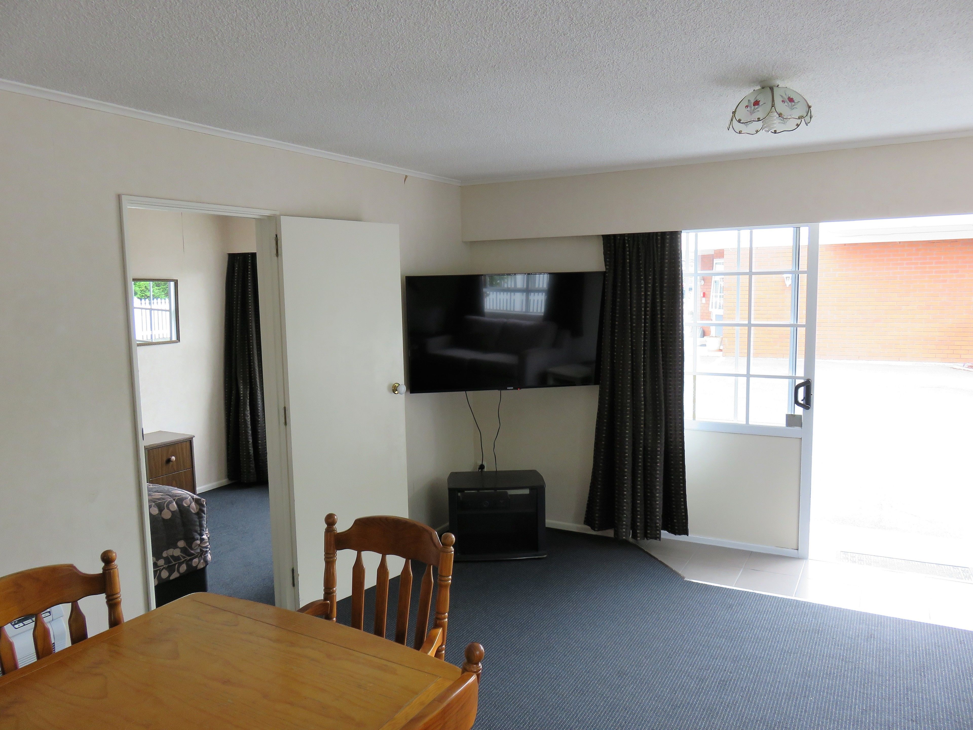 A room with a dining table, chairs, a television mounted on the wall, and a sliding glass door leading to an outdoor area.