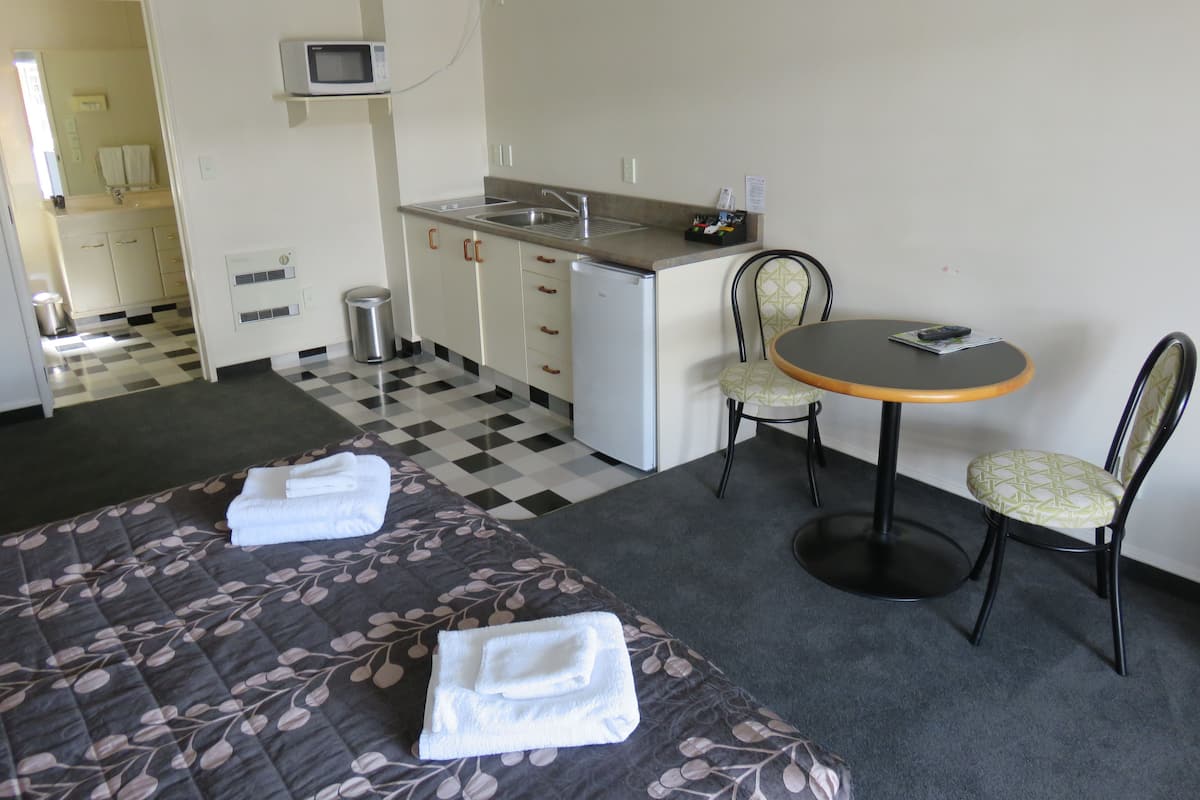 A hotel room with two beds, a small kitchenette, a dining area with a table and chairs, and a checkered floor.