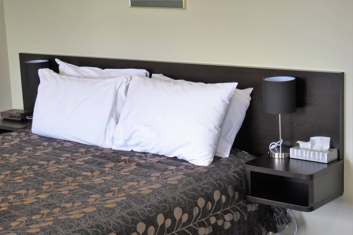 A neatly made bed with white pillows and a patterned bedspread, a bedside table with a lamp, and a tissue box.