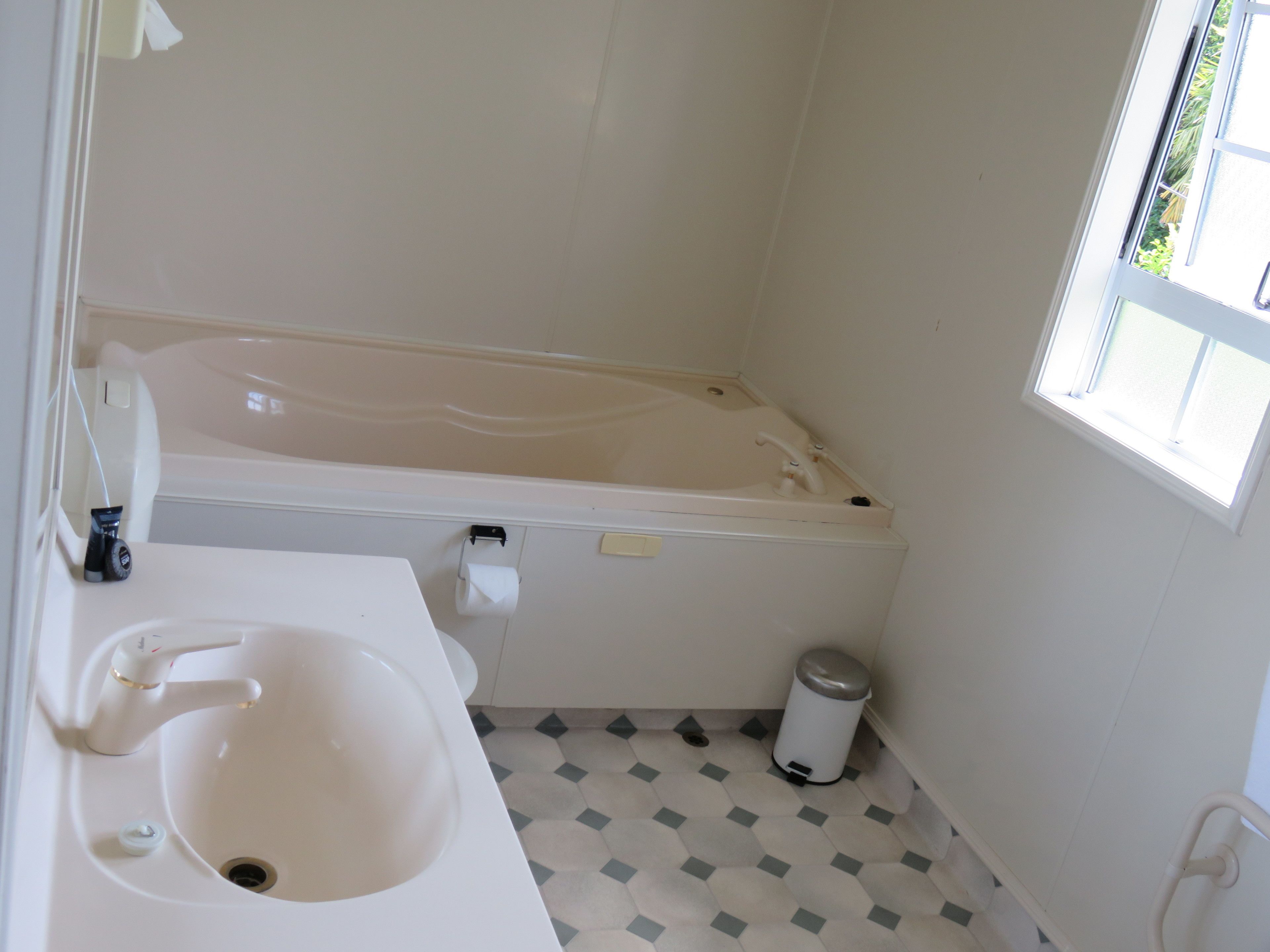 Een badkamer met bad, wastafel, toilet en een raam.
