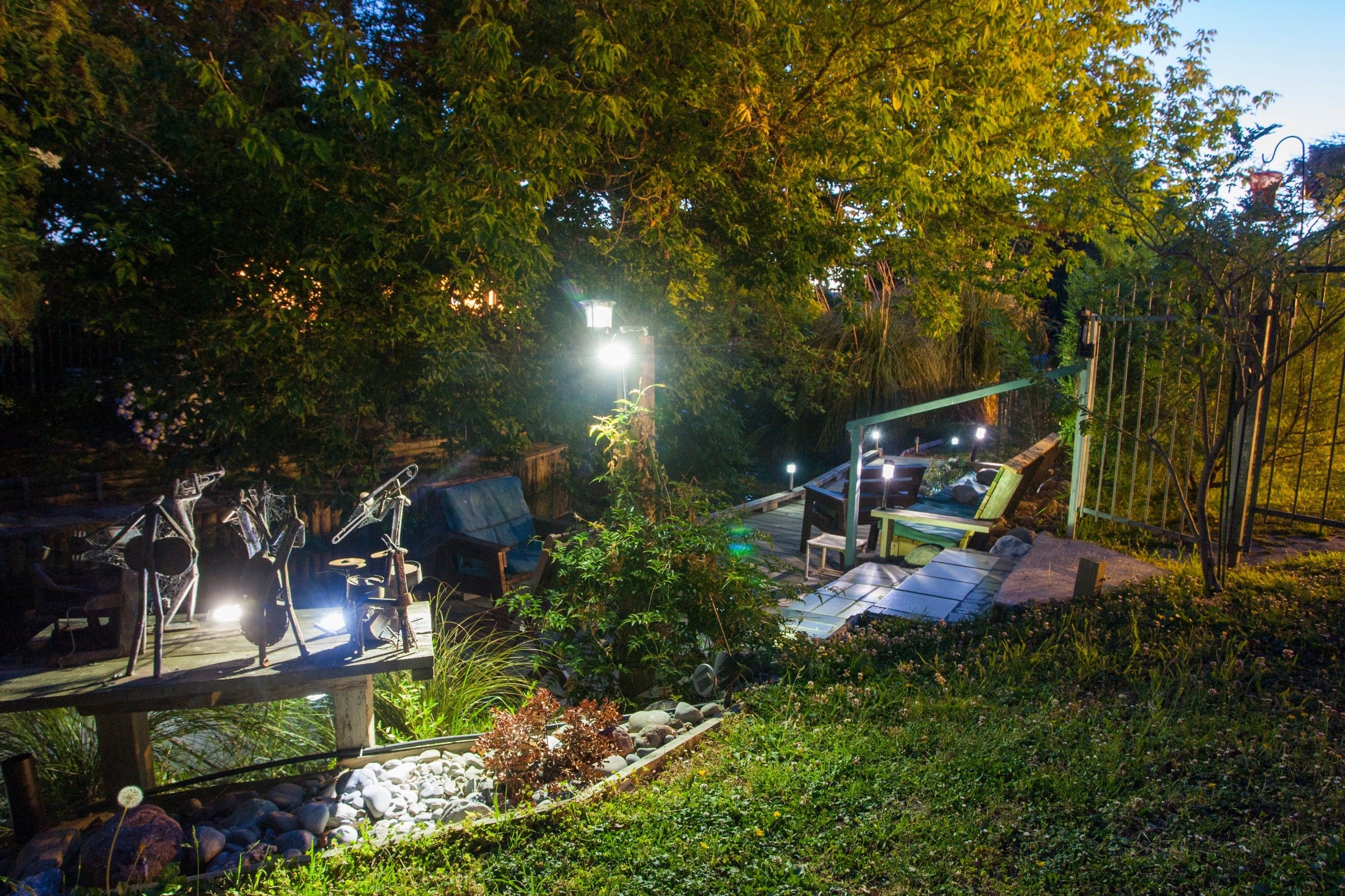 A garden with a wooden deck, metal sculptures, and a well-lit pathway.