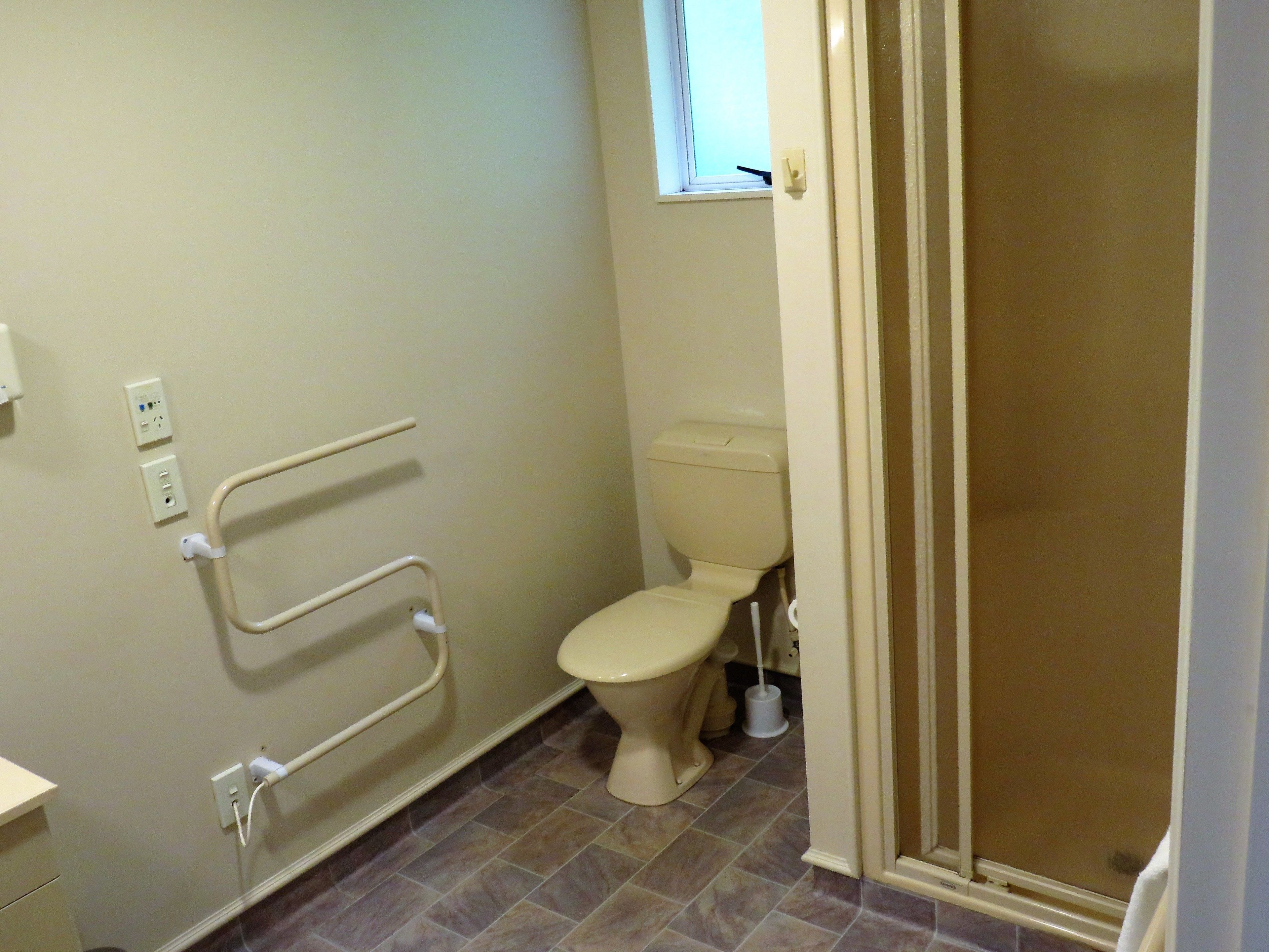 Une salle de bain équipée de toilettes, de barres d’appui et d’un espace douche.