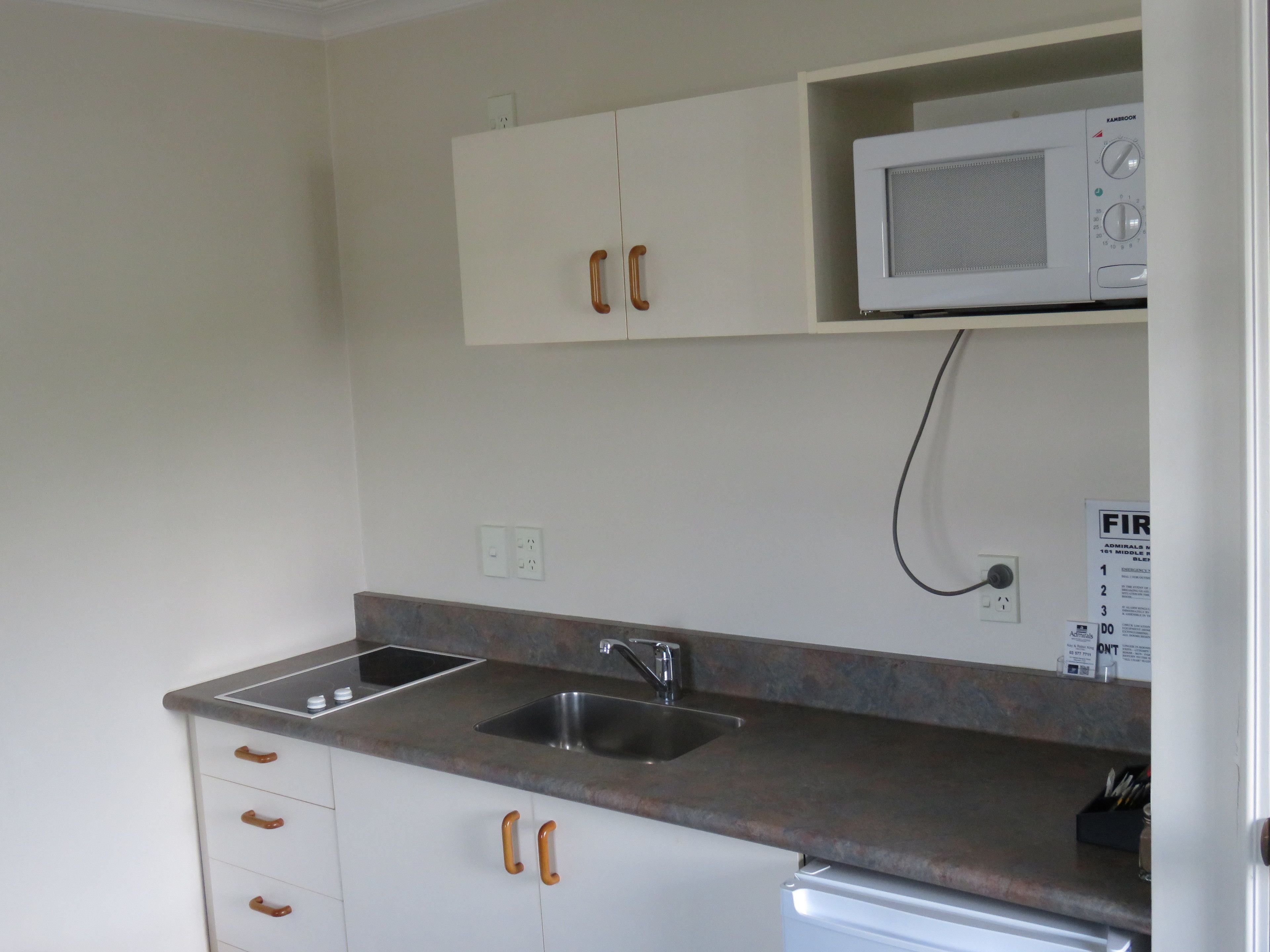 A kitchen with two sinks, wooden handles on the cabinets, a microwave, and a power outlet.