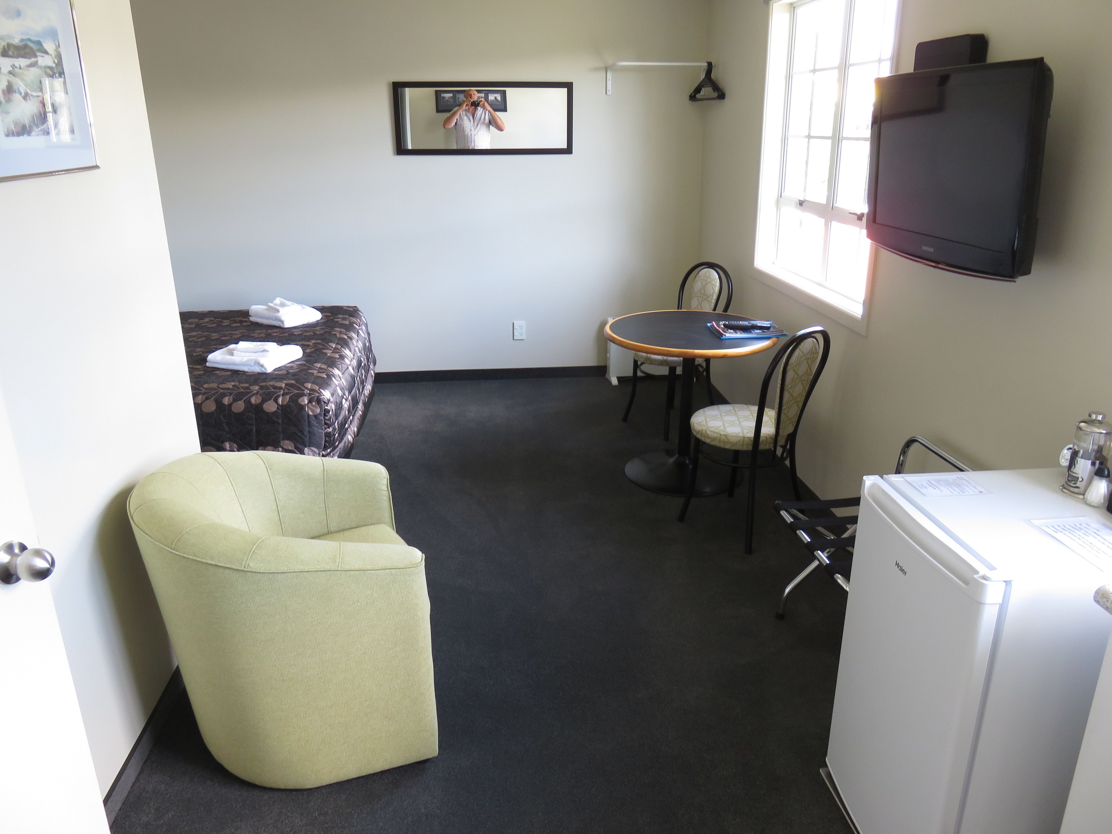 Una habitación compacta con cama, una pequeña mesa con sillas, un refrigerador y un televisor.