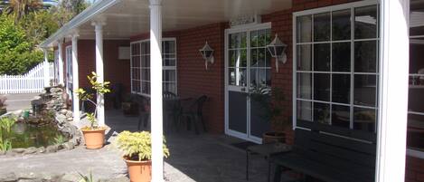 A covered patio with a stone floor, potted plants, a small pond, and a bench.