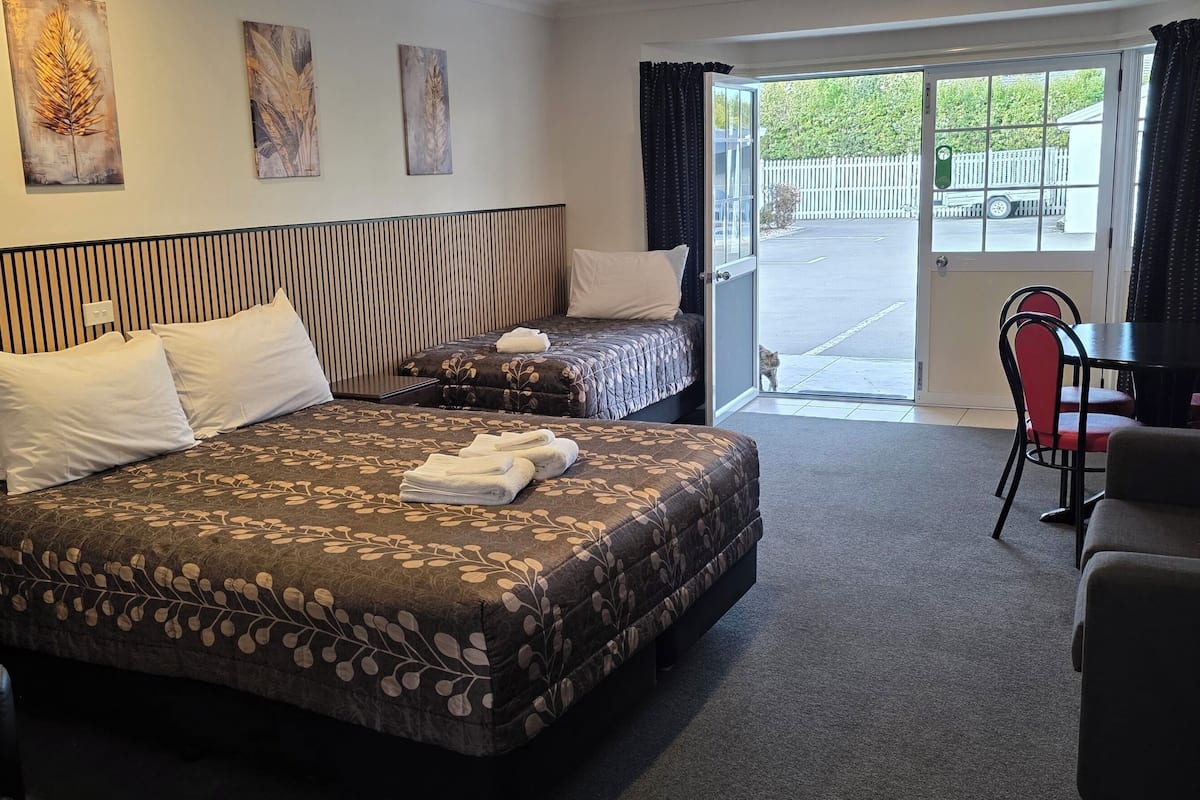 A hotel room with a bed, a sofa, a dining table with chairs, and a sliding door to the outside.