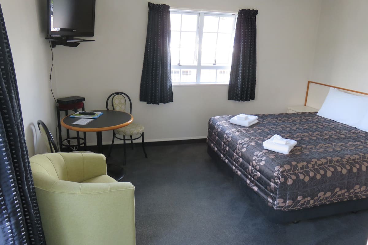 A hotel room with a bed, a chair, a small table, a television, and a window with curtains.