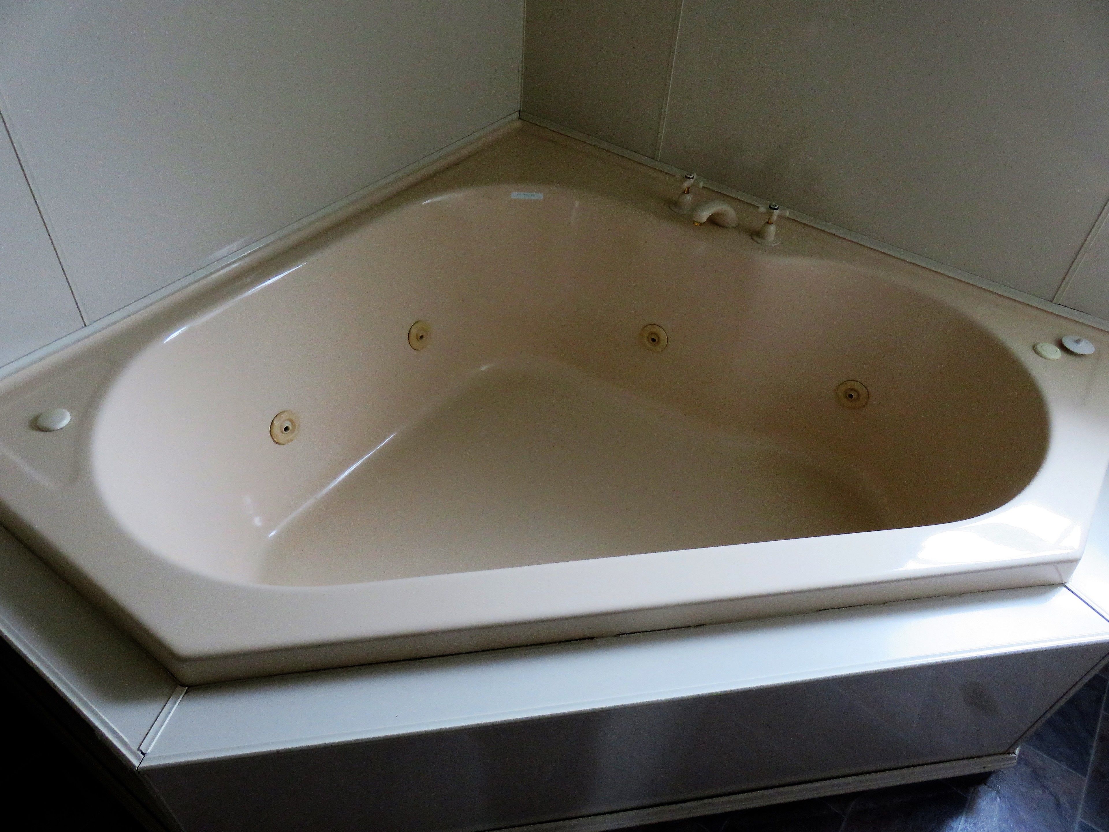 A rectangular bathtub with a single faucet and a drain plug, set in a corner with white tiled walls.