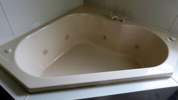 A rectangular bathtub with a single faucet and a drain plug, set in a corner with white tiled walls.