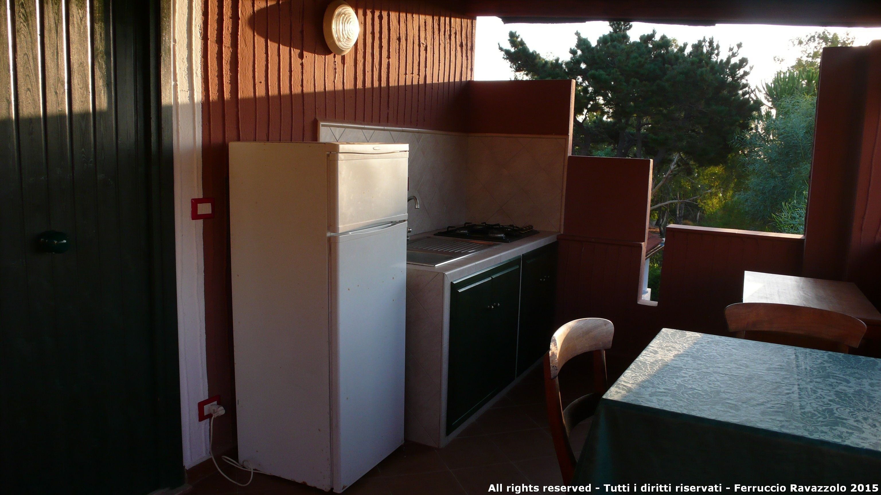 Een compacte keuken met een koelkast, fornuis en wastafel, een kleine eettafel en een stoel.