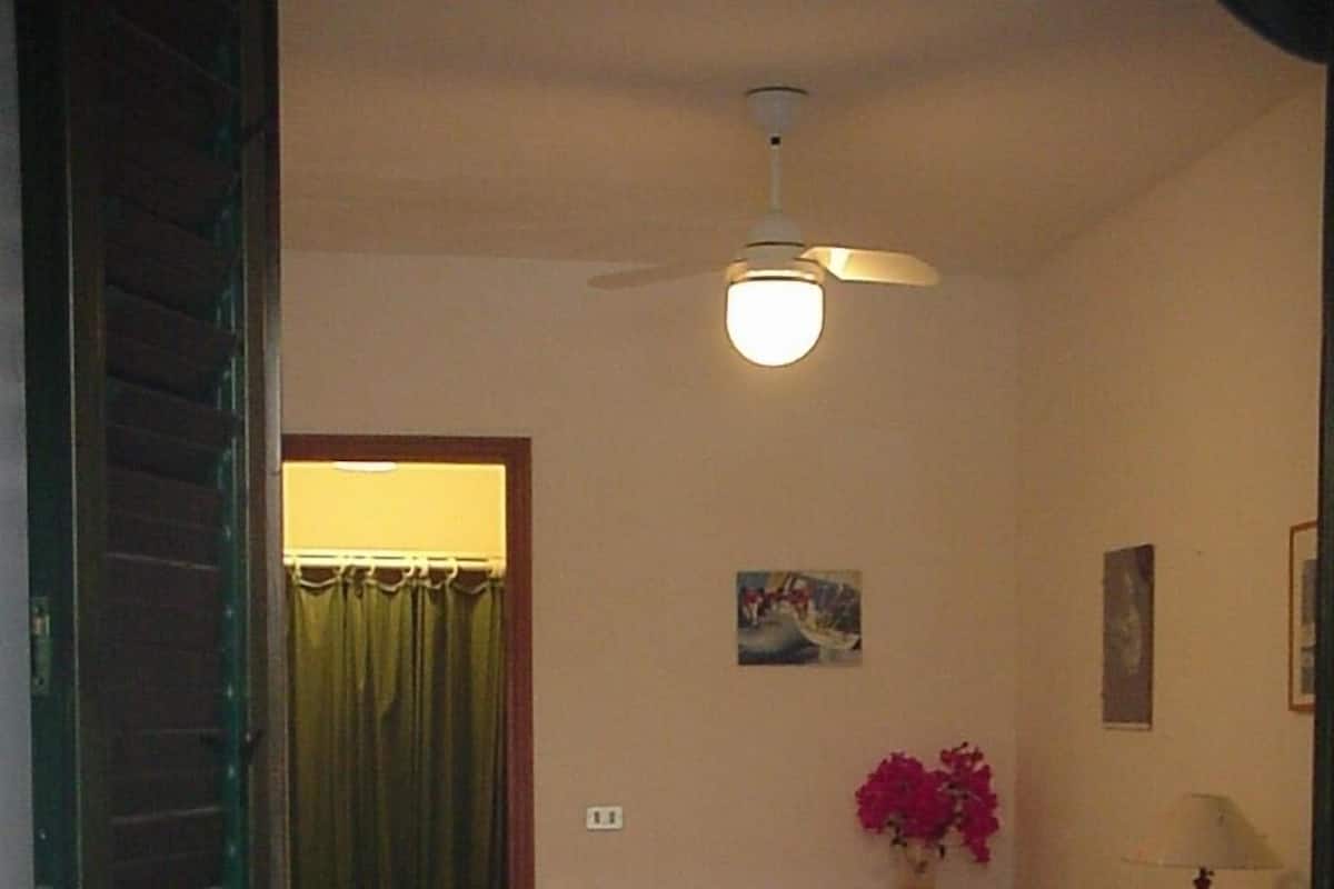 A bedroom with two beds, a ceiling fan, a nightstand, a lamp, and a painting on the wall.
